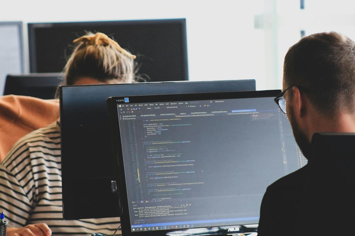 Dos personas programando frente a varios monitores en una oficina
